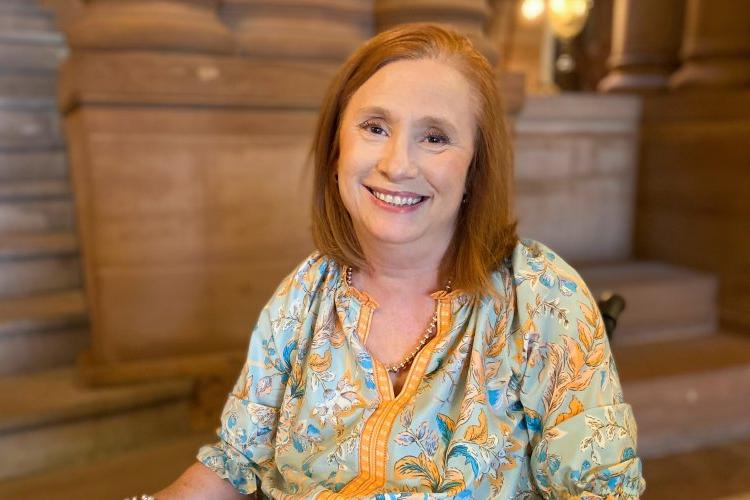 金伯利山, 红头发，蓝黄色衬衫, sits in her wheelchair inside the capital building in Albany, 微笑.